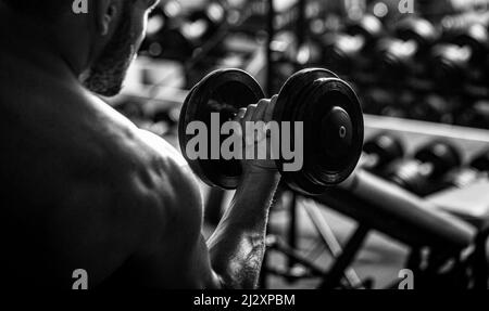 Homme bodybuilder faisant des exercices avec des haltères. Bodybuilder s'entraîner avec des haltères à la salle de gym Banque D'Images