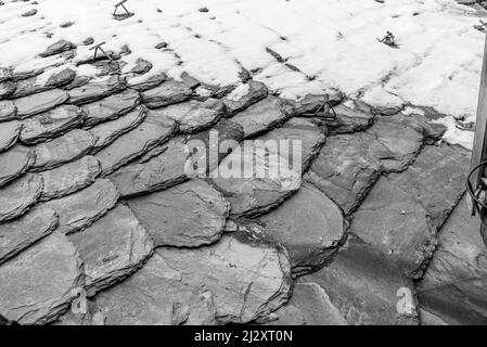 Anciennes tuiles de toit grises, partiellement couvertes de neige, d'arrière-plan, monochromes, noir et blanc. Banque D'Images