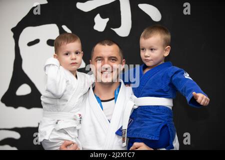 École de Judo pour enfants. L'entraîneur de judo tient dans ses bras de petits élèves de kimano. Banque D'Images