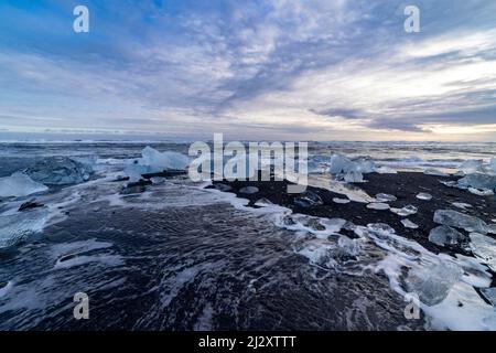 Petits blocs de glace et vagues sur Diamond Beach avec sable noir, Breidamerkursandur, Islande Banque D'Images