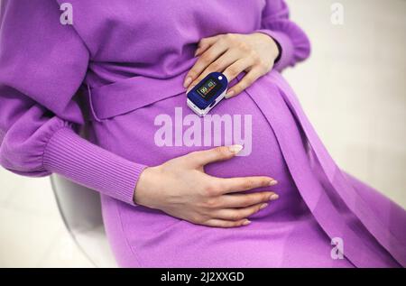 Femme enceinte avec oxymètre de pouls sur le doigt.Médecin mesurant le niveau de saturation en oxygène lors de la visite d'une mère enceinte atteinte de coronavirus au hom Banque D'Images