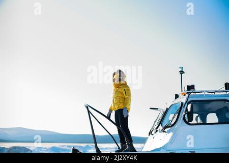 Lac Baikal en février. Les touristes féminins voyagent sur un aéroglisseur Hivus à travers le détroit de la petite mer gelé. Magnifique paysage d'hiver. Femme en jaune Banque D'Images