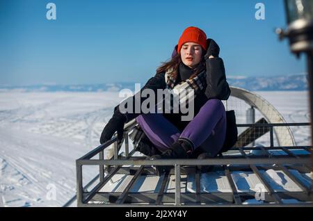 Lac Baikal en février. Les touristes féminins voyagent sur un aéroglisseur Hivus à travers le détroit de la petite mer gelé. Magnifique paysage d'hiver. Femme en rouge ha Banque D'Images