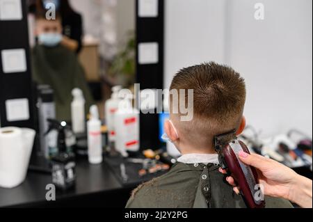 Coupe de cheveux pour enfants dans la barbershop, coupe de cheveux élégante et moderne pour les écoliers, travail pendant la pandémie, coupe de cheveux pour enfants avec des ciseaux. Banque D'Images