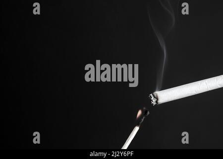 allumer une cigarette avec un allumette brûlante sur fond sombre. Banque D'Images