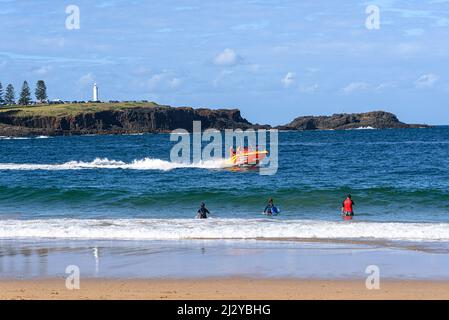 Les gens de Kendalls Beach regardent un bateau de sauvetage Kiama Surf aller près de la rive avec Blowhole point en arrière-plan Banque D'Images