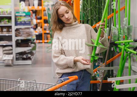 Femme choisit un outil de forage de jardin manuel dans le magasin de matériel dans le département agricole. Cultivateur de jardin creuseur de trou manuel Banque D'Images