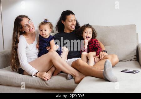 famille heureuse caucasienne assise sur le canapé faisant des visages drôles, maman et papa assis jouant avec leurs filles dans le salon, concept de style de vie. Banque D'Images