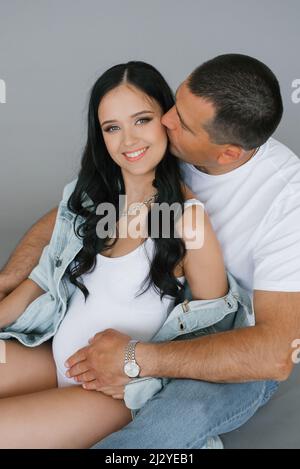 Un homme heureux encadre sa petite amie enceinte et regarde dans l'appareil photo. Le mari aimant embrasse doucement la femme enceinte en attendant un bébé Banque D'Images