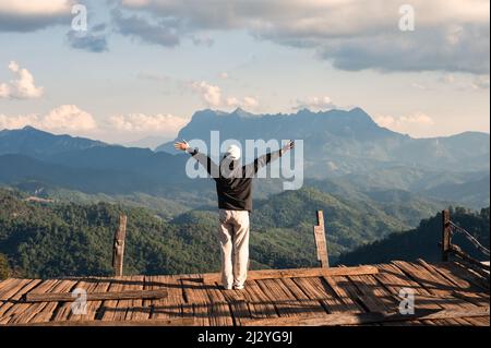 Vue arrière gaie d'une femme asiatique debout bras levés sur un balcon en bois avec sommet de montagne dans la campagne à Chiang Mai, Thaïlande Banque D'Images