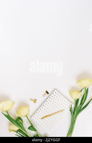 Bureau pour femmes à poser à plat avec bloc-notes, bouquet de fleurs jaunes de printemps, accessoires. Vue sur le dessus de la table des fêtes pour femmes et espace de copie Banque D'Images