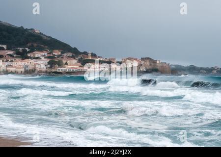 Les mers agitées se sont écraées sur la plage d'Algajola dans la région de Balagne en Corse avec village et citadelle au loin Banque D'Images