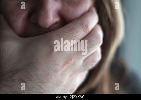 Gros plan d'une femme qui pleure et de la main d'un homme couvrant sa bouche, une scène de violence sexuelle. Banque D'Images