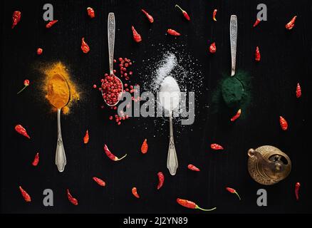 Différents types d'épices sur fond noir dans des cuillères à thé. Vue de dessus sur le curcuma, le poivre rouge, le piment, le sel et la spiruline en poudre Banque D'Images