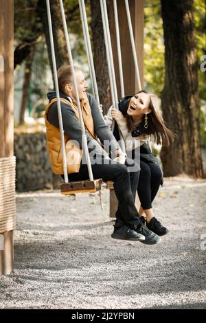 Joyeux couple joyeux en automne dans le parc de la forêt dans l'après-midi sur une balançoire en bois. Photo de haute qualité Banque D'Images
