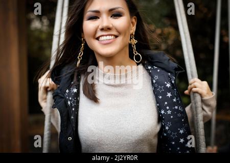 Portrait d'une jeune femme asiatique heureuse avec un sourire blanc neige balançant sur un balancement extérieur. Banque D'Images
