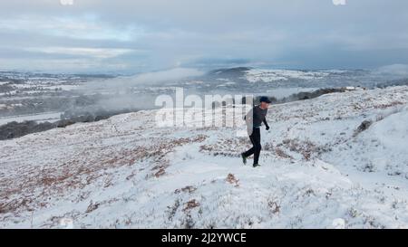 Le coureur de fond apprécie les landes enneigées tandis que la neige couvre le village de Burley-in-Wharfedale faisant de Burley Moor un pays merveilleux d'hiver, West Yorkshire, Angleterre Banque D'Images