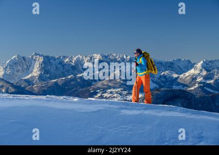 Une femme qui fait de la randonnée avec des raquettes sur son sac à dos va sur la piste de neige, les montagnes Kaiser en arrière-plan, Hochgern, les Alpes de Chiemgau, la haute-Bavière, la Bavière, Allemagne Banque D'Images