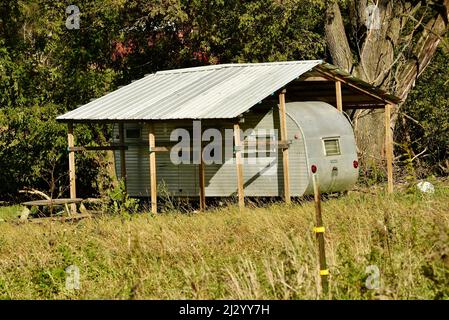 Remorque de camping vintage en métal argenté, branchée et élégante, garée sous un toit en métal protecteur dans un emplacement isolé, sur une colline de ferme sous les arbres, Osseo, Wisconsin, États-Unis Banque D'Images