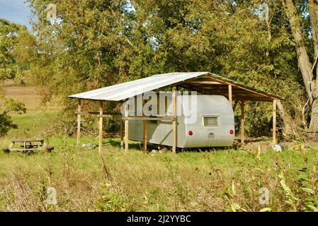 Remorque de camping vintage en métal argenté, branchée et élégante, garée sous un toit en métal protecteur dans un emplacement isolé, sur une colline de ferme sous les arbres, Osseo, Wisconsin, États-Unis Banque D'Images