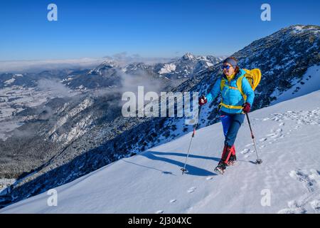 Une femme qui fait de la randonnée avec des raquettes dans son sac à dos va sur une pente de montagne enneigée, Alpes bavaroises en arrière-plan, Jägerkamp, Spitzing, Alpes bavaroises, haute-Bavière, Bavière, Allemagne Banque D'Images