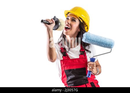 Un jeune peintre gai en vêtements de travail chante et utilise un pinceau comme microphone. Concept drôle sur fond blanc isolé. Banque D'Images