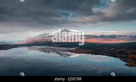 Paysage avec des montagnes enneigées et reflet dans le lac dans le parc national Stora Sjöfallet en automne en Laponie en Suède d'en haut Banque D'Images