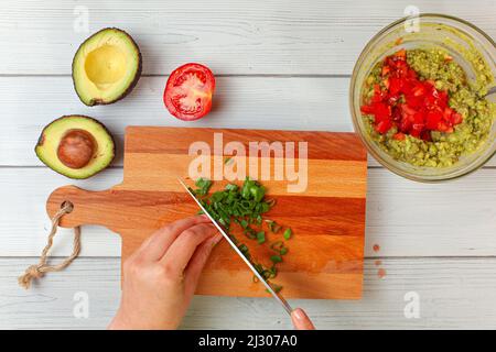 Tranches d'avocat, tomates, oignons de printemps en tranches à la main - ingrédients de base de guacamole sur le plan de travail, vue d'en haut Banque D'Images