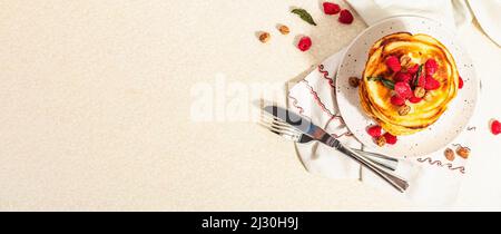 Crêpes américaines maison classiques avec framboises surgelées, noisettes et menthe. Petit déjeuner sain, couverts, fond en béton de pierre légère. Har. Tendance Banque D'Images