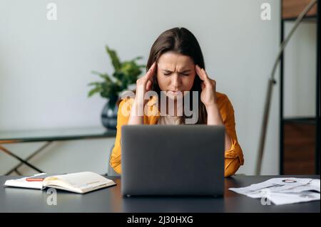 Jeune femme d'affaires, Manager, indépendant ou secrétaire caucasienne, fatiguée de s'asseoir au travail à un ordinateur portable, de masser les temples, de fermer les yeux, a besoin d'un repos Banque D'Images