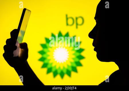 Dans cette illustration, la silhouette d'une femme tient un smartphone avec le logo British Petroleum (BP) en arrière-plan. Banque D'Images