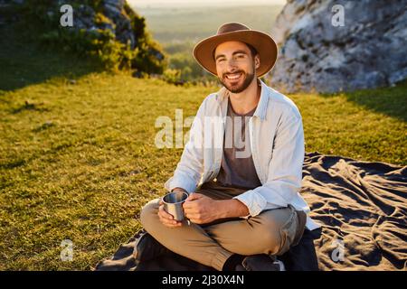 Portrait d'un jeune homme avec une tasse assise sur une couverture en montagne pendant la randonnée estivale dans le Jura Pologne Banque D'Images