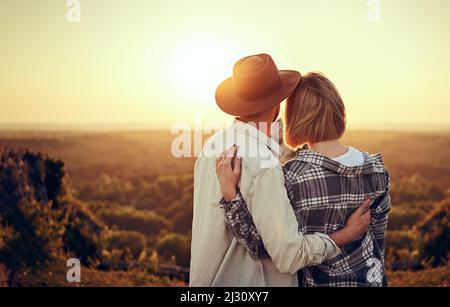 Un jeune couple regarde le coucher du soleil s'embrassant dans la nature pendant la randonnée estivale Banque D'Images