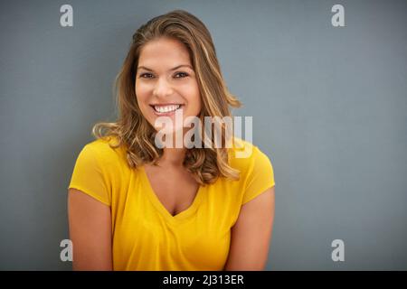 Shes heureux-Go-chanceux. Photo d'une jeune femme posant contre un mur gris. Banque D'Images