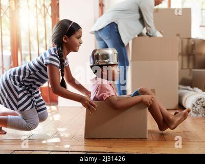 Vous remplissez déjà leur nouvelle maison avec des tonnes de plaisir. Photo de deux petits frères et sœurs jouant avec une boîte en carton tout en déplaçant la maison. Banque D'Images