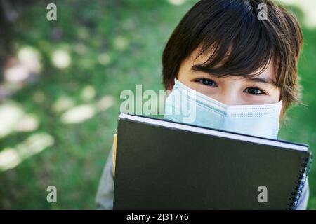 Deux choses que vous ne devriez jamais oublier. Photo d'un petit garçon portant un masque et tenant des livres dans la nature. Banque D'Images