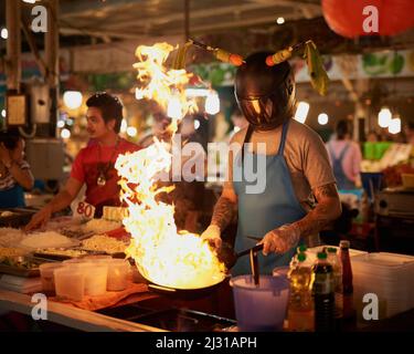 Des trucs chauds. Photo d'un vendeur d'aliments non identifiable portant un casque tout en flamant quelque chose dans une casserole. Banque D'Images