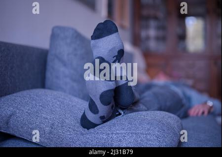 Homme allongé sur un canapé dans le salon avec des chaussettes chaudes Banque D'Images
