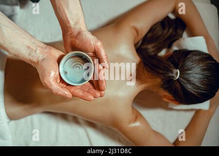 Homme de masseuse bol de maintien avec huile chaude infusée aux herbes pour le massage du dos Banque D'Images