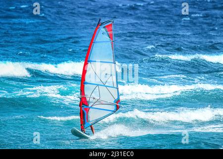 sports nautiques : une surfeuse à voile rouge et bleu à cheval sur la vague pendant une journée d'été venteuse Banque D'Images