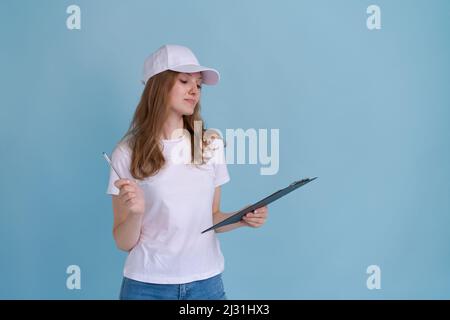 Profession, travail et personnes concept - heureuse femme souriante de livraison en uniforme blanc avec porte-document stylo sur fond bleu. Promoteur de fille caucasienne dans le football blanc et la casquette Banque D'Images