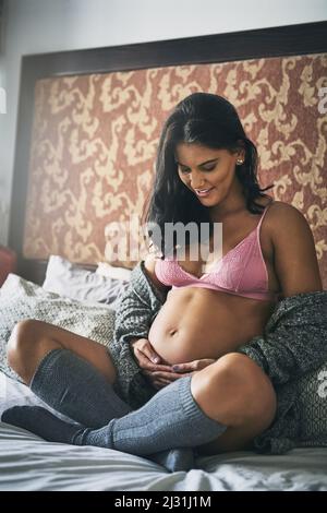 Elle peut dire que sa bayes va être en bonne santé. Prise de vue en longueur d'une jeune femme enceinte attrayante assise sur son lit à la maison. Banque D'Images
