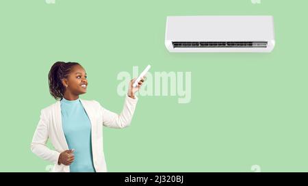 Femme avec télécommande debout près du climatiseur isolé sur fond vert clair. Banque D'Images