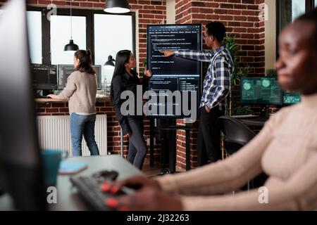 Développeur de réseau back-end afro-américain expliquant aux collaborateurs les lignes de code de l'application. Équipe développant des couches de sécurité supplémentaires afin de maintenir une bonne fonctionnalité du système. Banque D'Images