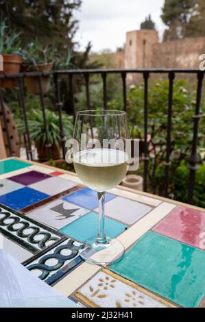 Verre de vin blanc sec espagnol servi sur la terrasse extérieure avec vue sur les murs rouges de la forteresse andalouse médiévale Alhambra à Grenade, Espagne Banque D'Images