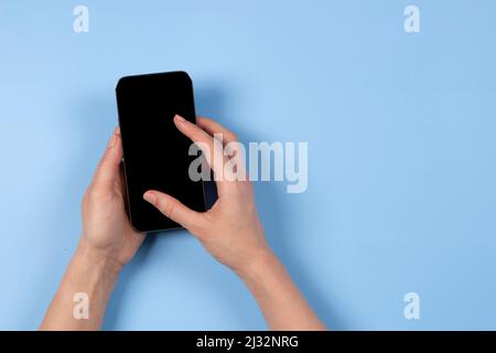 Main féminine touchant l'écran du smartphone, utilisation de l'application, navigation sur Internet, achats en ligne, arrière-plan bleu clair avec espace de copie pour le texte Banque D'Images