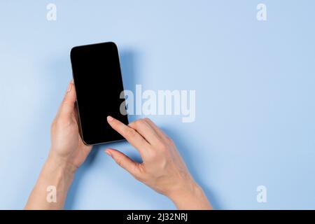 Main féminine touchant l'écran du smartphone et pointant avec l'index sur l'écran vierge du téléphone mobile sur fond bleu clair Banque D'Images