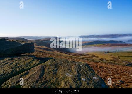 Haut sur les rochers de pierre à aiguiser de Stanage Edge en regardant vers le bas les vallées remplies de brume de Derbyshire. Banque D'Images