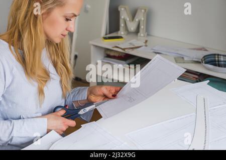 La couturière coupe des motifs de paper pour la robe avec des ciseaux. Développement de conception et création de vêtements Banque D'Images