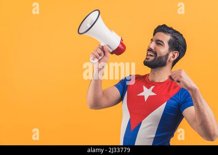 Un homme à barbe latine vêtu d'un t-shirt drapeau cubain criant au mégaphone sur fond de studio orange. Photo de haute qualité Banque D'Images